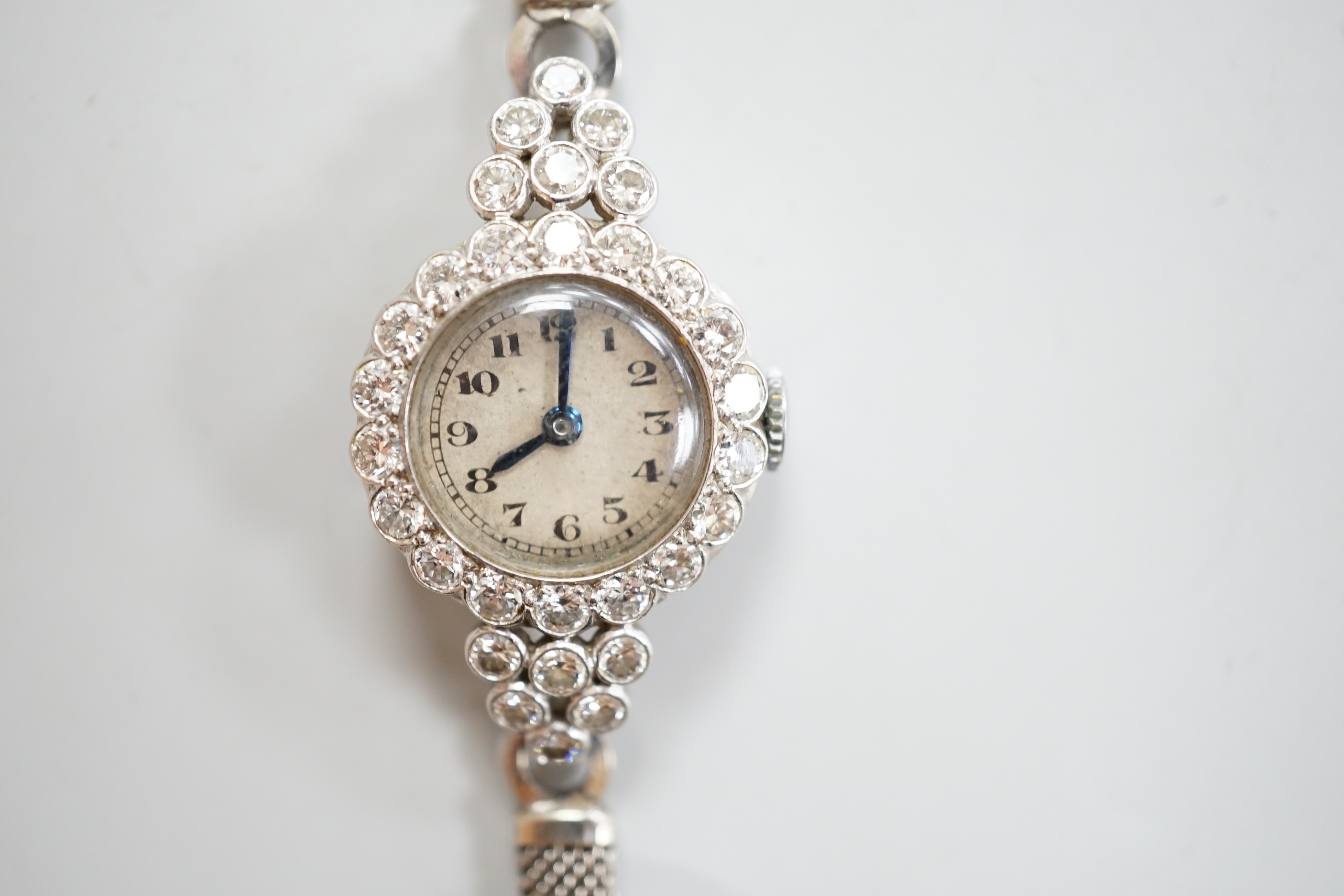 A lady's white metal and diamond set Movado manual wind cocktail watch, on a diamond set 9ct white metal mesh link bracelet, gross weight 18 grams.